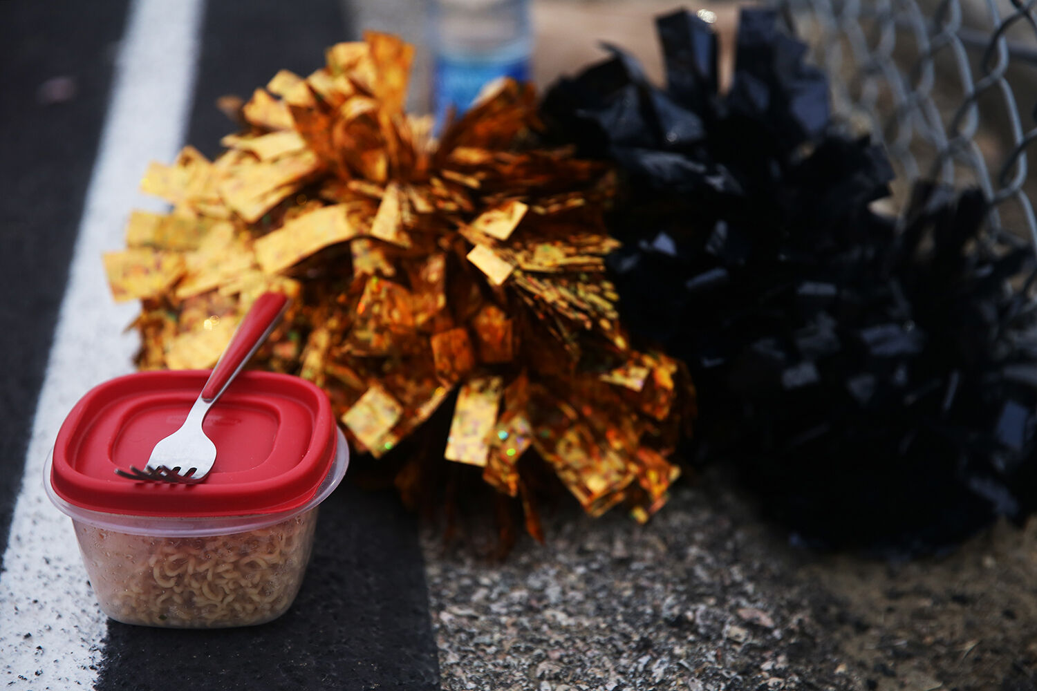 A tupperware of ramen sits next to a set of pompoms on the track